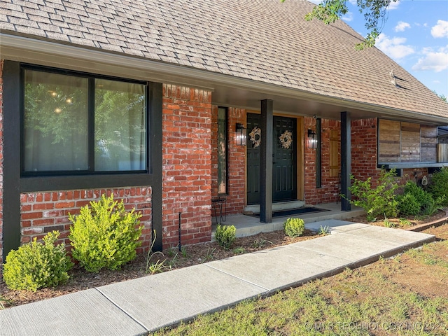 property entrance with a shingled roof and brick siding