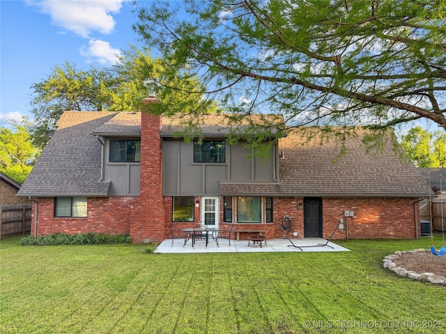 rear view of house with a shingled roof, a patio, a chimney, brick siding, and central AC unit