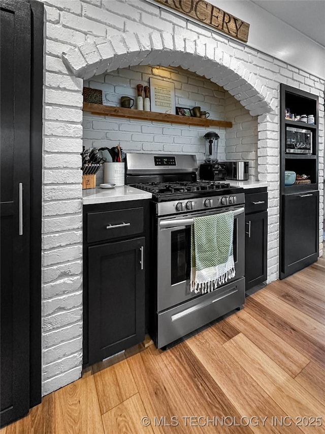 kitchen featuring stainless steel range with gas cooktop, light wood-style flooring, light countertops, and dark cabinets