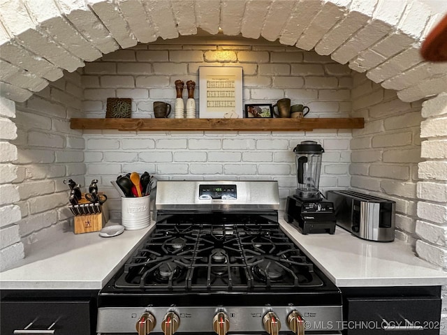 kitchen featuring gas stove, open shelves, light countertops, and brick wall