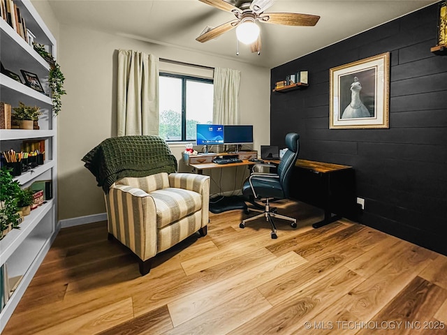 office area with wood finished floors, a ceiling fan, and an accent wall