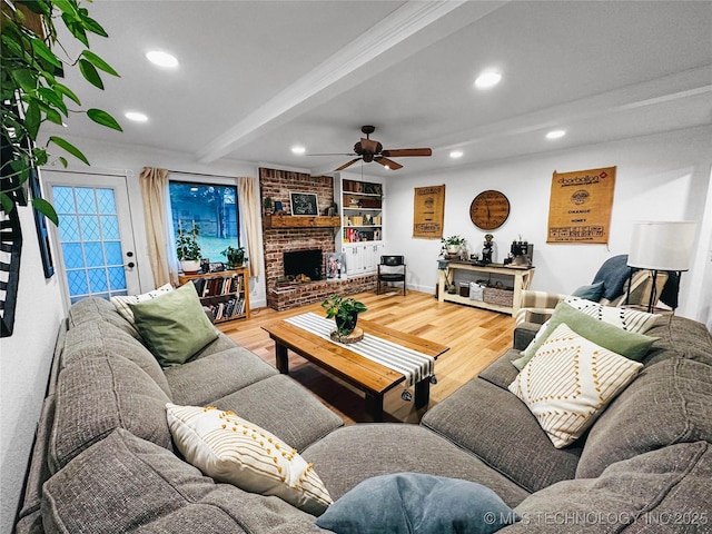 living area with beam ceiling, a ceiling fan, wood finished floors, recessed lighting, and a brick fireplace