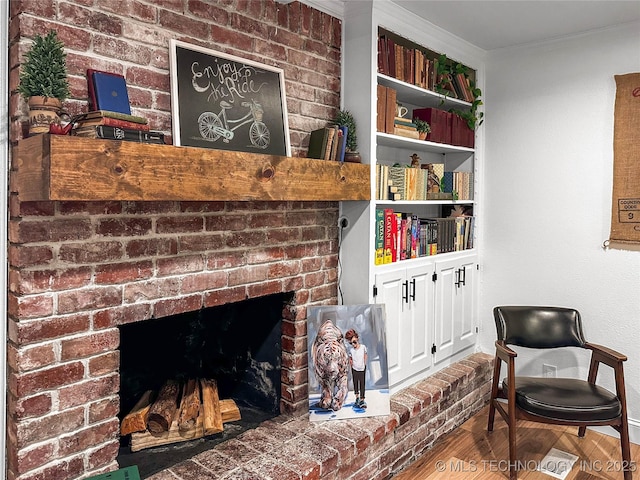 sitting room featuring wood finished floors, a brick fireplace, baseboards, and crown molding