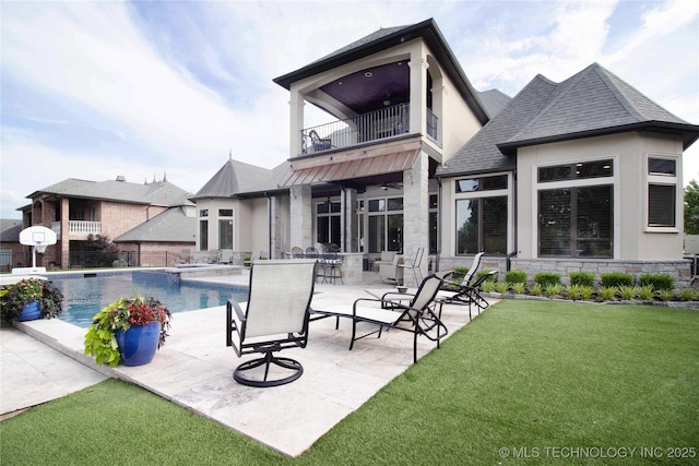 rear view of house featuring a balcony, stone siding, a patio, a shingled roof, and stucco siding