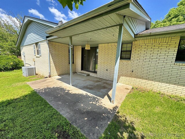 rear view of house with a lawn, brick siding, an attached carport, and a patio area