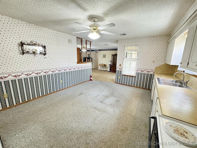 kitchen featuring wallpapered walls, a sink, ceiling fan, light colored carpet, and light countertops