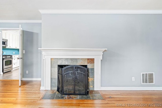 detailed view of appliances with stainless steel finishes, ornamental molding, wood finished floors, a tiled fireplace, and baseboards