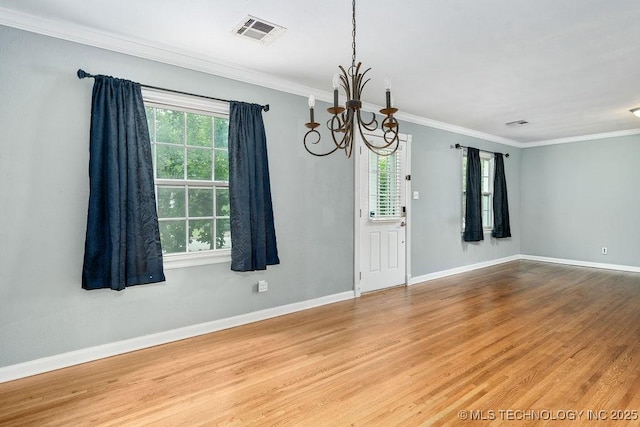empty room with a chandelier, wood finished floors, crown molding, and baseboards