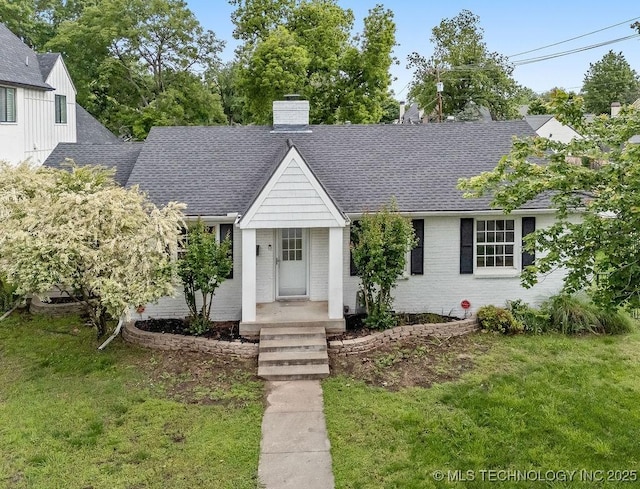 view of front of home featuring a chimney, roof with shingles, brick siding, and a front yard