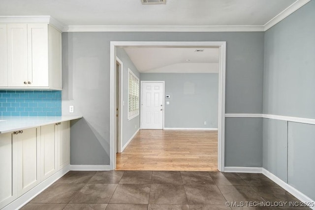 kitchen featuring backsplash, white cabinetry, crown molding, baseboards, and light countertops
