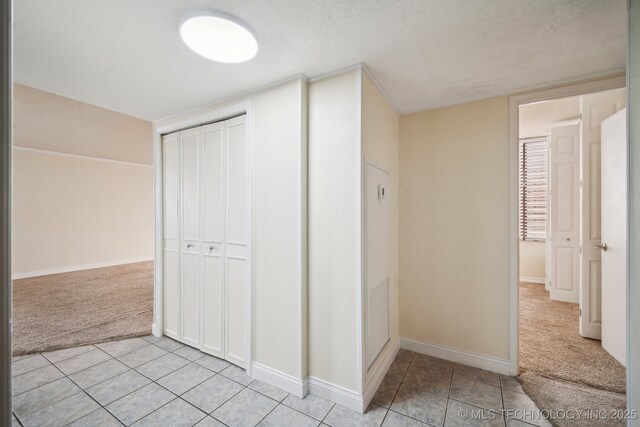 corridor with light carpet, light tile patterned flooring, baseboards, and a textured ceiling