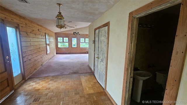 hall with vaulted ceiling, wood walls, a textured ceiling, and baseboards