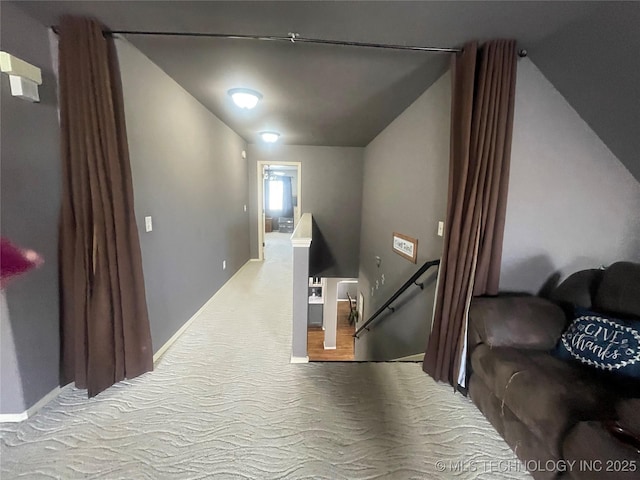 hall with an upstairs landing, vaulted ceiling, and carpet floors