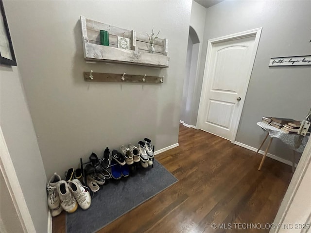foyer entrance with arched walkways, dark wood finished floors, and baseboards