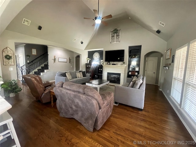 living room with arched walkways, ceiling fan, a glass covered fireplace, dark wood-type flooring, and high vaulted ceiling