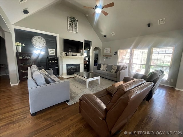 living area with a ceiling fan, arched walkways, high vaulted ceiling, wood finished floors, and a glass covered fireplace
