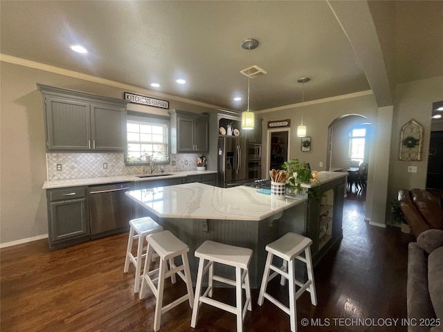 kitchen featuring appliances with stainless steel finishes, gray cabinets, arched walkways, a sink, and backsplash