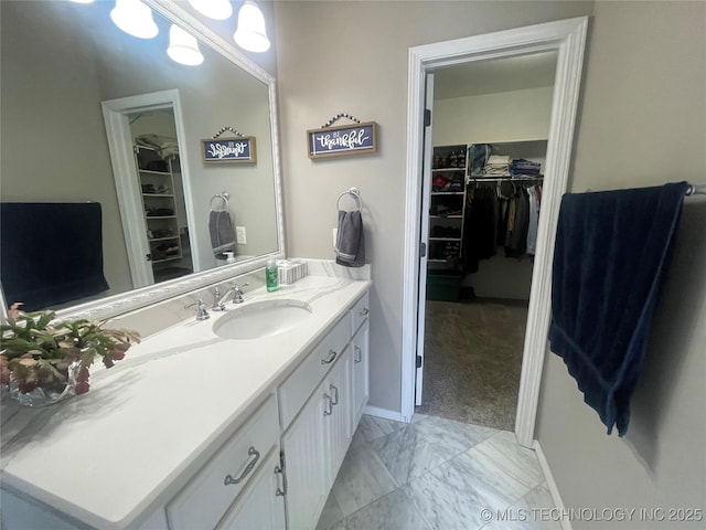 bathroom featuring marble finish flooring, vanity, a spacious closet, and baseboards