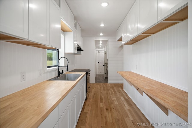 kitchen with a sink, butcher block countertops, electric range, light wood-type flooring, and white cabinets