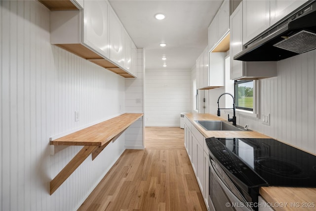 kitchen featuring stainless steel electric range, under cabinet range hood, a sink, light wood-type flooring, and white cabinetry