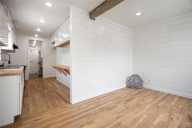 spare room with light wood-type flooring, wooden walls, a sink, beamed ceiling, and recessed lighting