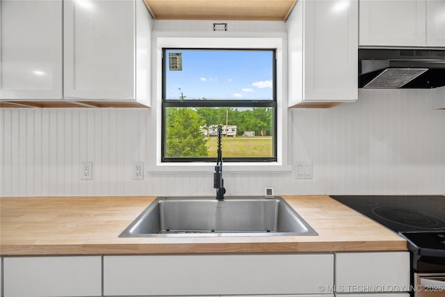 kitchen with wood counters, under cabinet range hood, a sink, electric range oven, and white cabinets