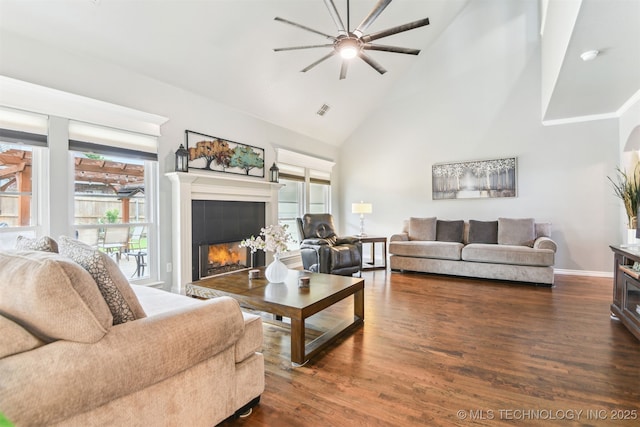 living room with a ceiling fan, a tiled fireplace, dark wood-type flooring, high vaulted ceiling, and baseboards