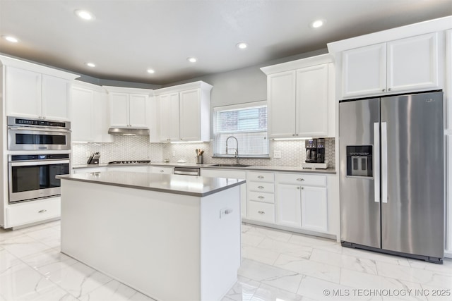 kitchen featuring appliances with stainless steel finishes, a sink, light marble finish floors, a center island, and white cabinetry