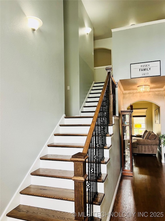 stairway with arched walkways, wood finished floors, baseboards, and ornamental molding
