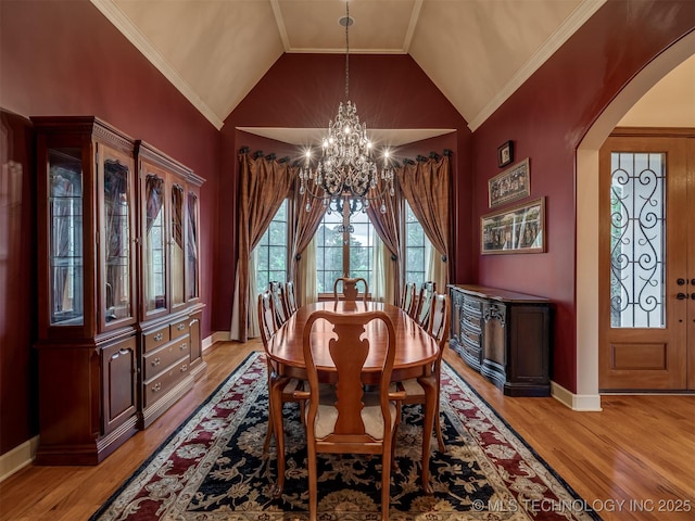 dining space with a chandelier, arched walkways, light wood-type flooring, vaulted ceiling, and baseboards