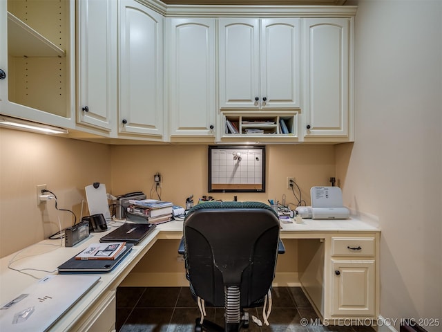 office area featuring built in study area, dark tile patterned floors, and baseboards
