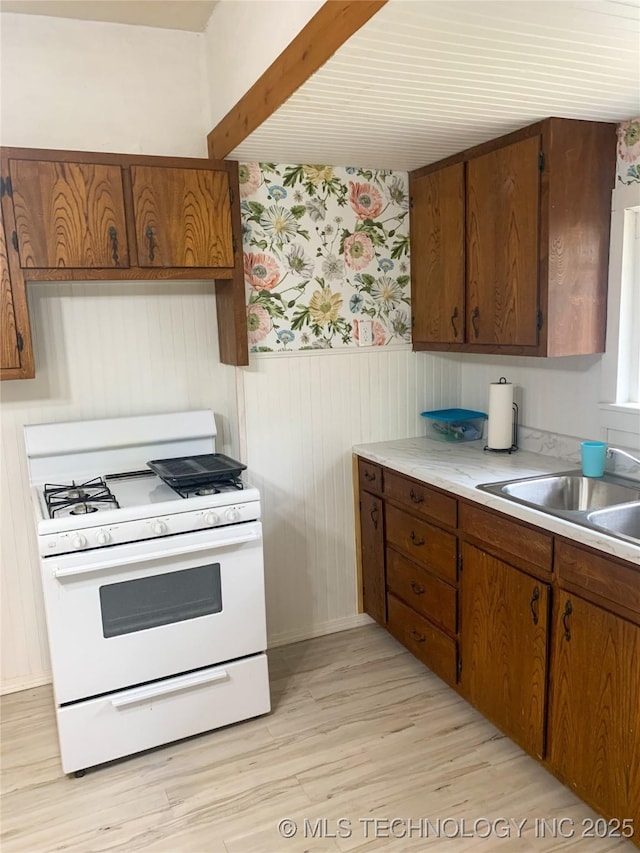 303 W Conklin, Sparks, OK 74869 - kitchen with white range with gas stovetop, wainscoting, light countertops, wallpapered walls, and light wood-style floors