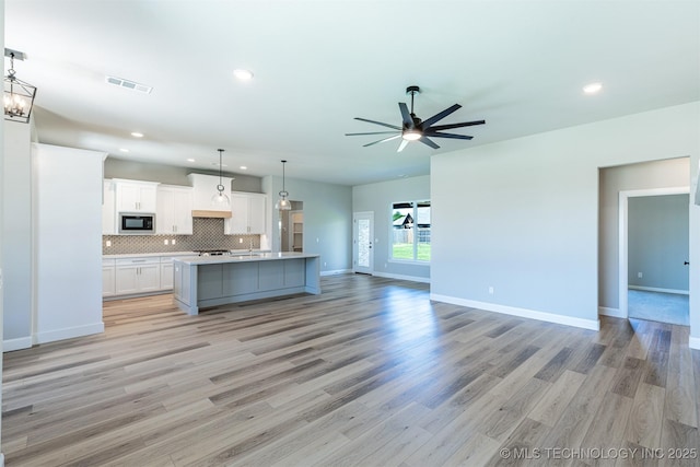 kitchen with black microwave, open floor plan, a ceiling fan, light countertops, and white cabinetry