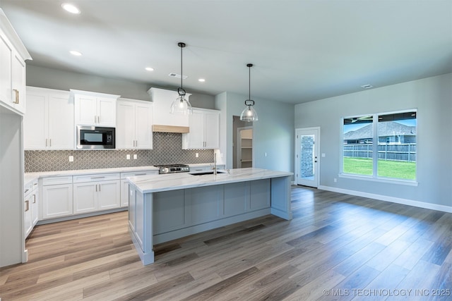 kitchen with black microwave, a sink, tasteful backsplash, light wood-type flooring, and recessed lighting