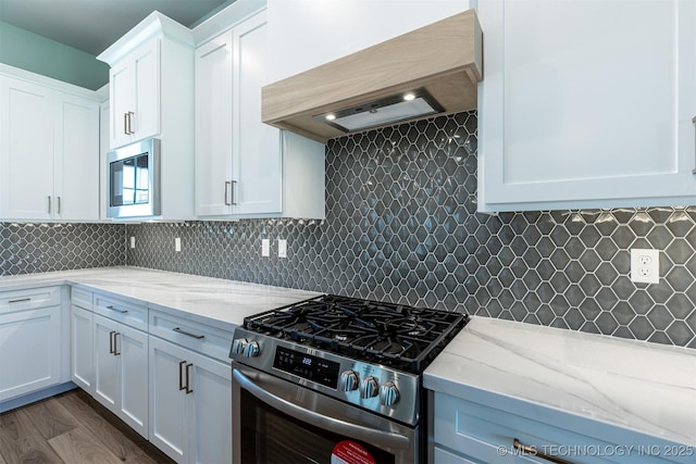 kitchen with appliances with stainless steel finishes, premium range hood, white cabinets, and light stone counters