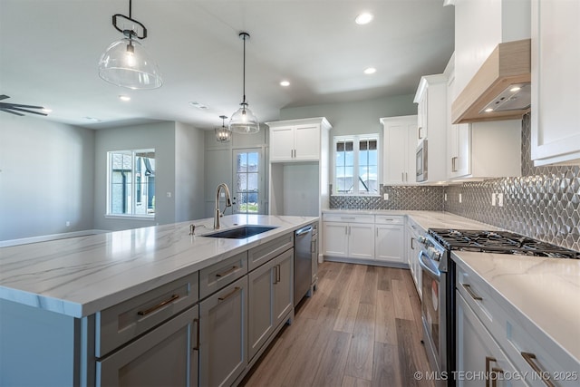 kitchen featuring stainless steel appliances, a sink, custom exhaust hood, light wood-style flooring, and white cabinets