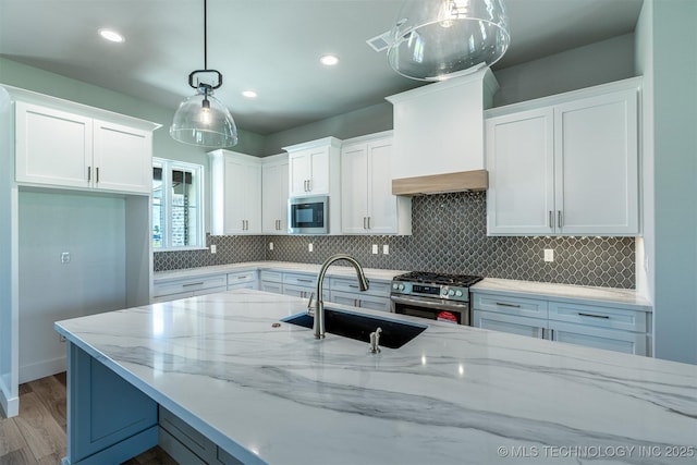 kitchen with stainless steel appliances, a sink, wood finished floors, white cabinetry, and light stone countertops
