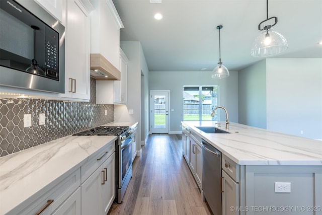 kitchen with a sink, appliances with stainless steel finishes, wood finished floors, white cabinetry, and backsplash
