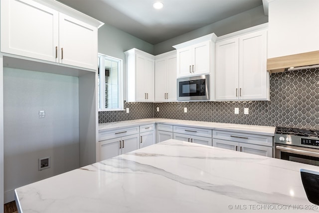kitchen with black microwave, stainless steel range with gas stovetop, white cabinets, and backsplash