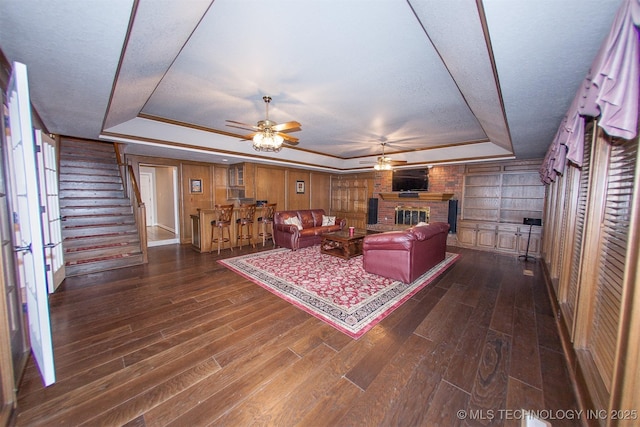 8734 S Richmond Ave, Tulsa, OK 74137 - living room featuring a tray ceiling, ceiling fan, a fireplace, dark wood finished floors, and stairs