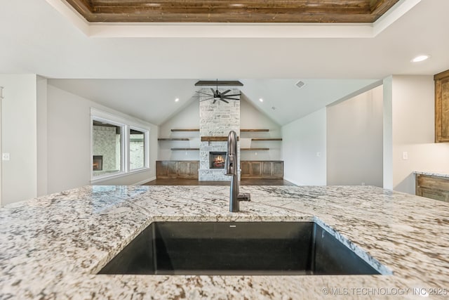 kitchen with a sink, a ceiling fan, a fireplace, wood finished floors, and light stone countertops
