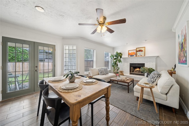 dining room featuring healthy amount of natural light, ceiling fan, french doors, ornamental molding, and a fireplace