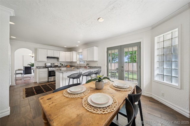 dining area featuring crown molding, french doors, dark wood-style floors, baseboards, and arched walkways