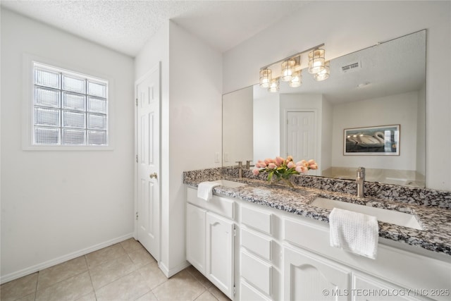 bathroom with tile patterned floors, baseboards, double vanity, and a textured ceiling