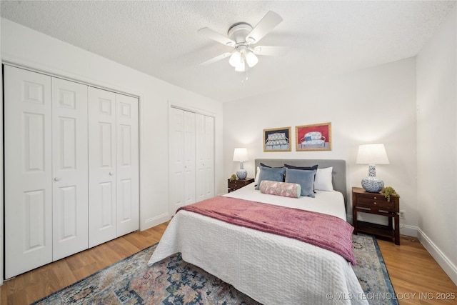 bedroom featuring wood finished floors, two closets, baseboards, ceiling fan, and a textured ceiling