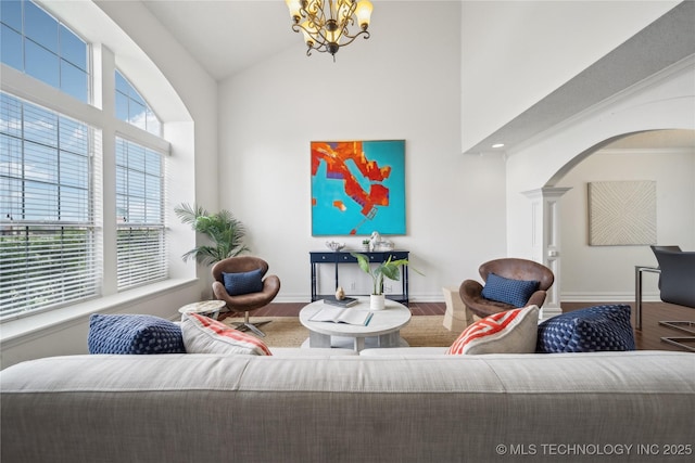 living room featuring wood finished floors, high vaulted ceiling, decorative columns, arched walkways, and a chandelier