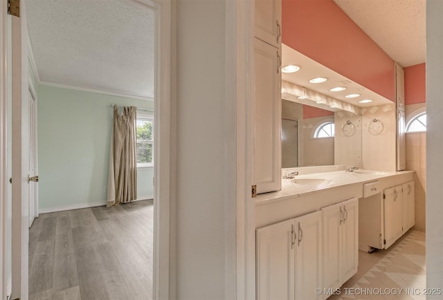 bathroom with a textured ceiling, vanity, wood finished floors, and ornamental molding