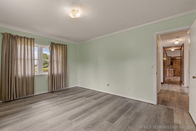 spare room with a textured ceiling, wood finished floors, ornamental molding, and baseboards