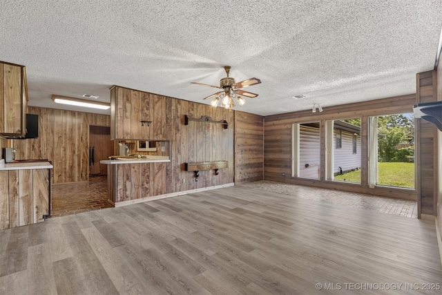 unfurnished living room with wooden walls, wood finished floors, ceiling fan, and a textured ceiling