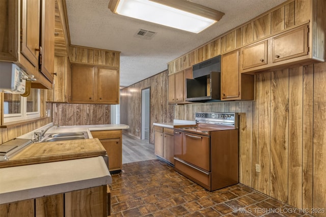 kitchen featuring electric stove, a sink, a textured ceiling, wooden walls, and light countertops